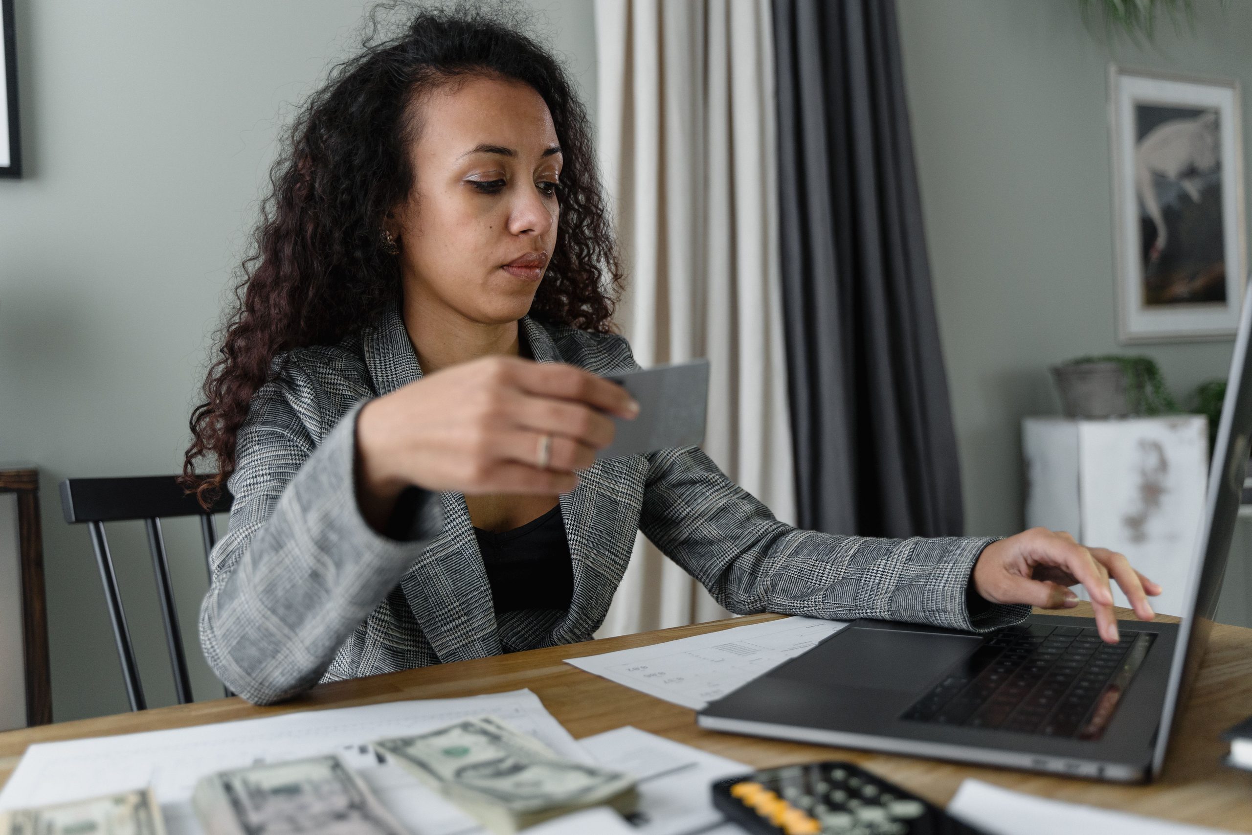 Mujer utilizando una tarjeta de crédito mientras revisa facturas, dinero y gastos desde su computadora.